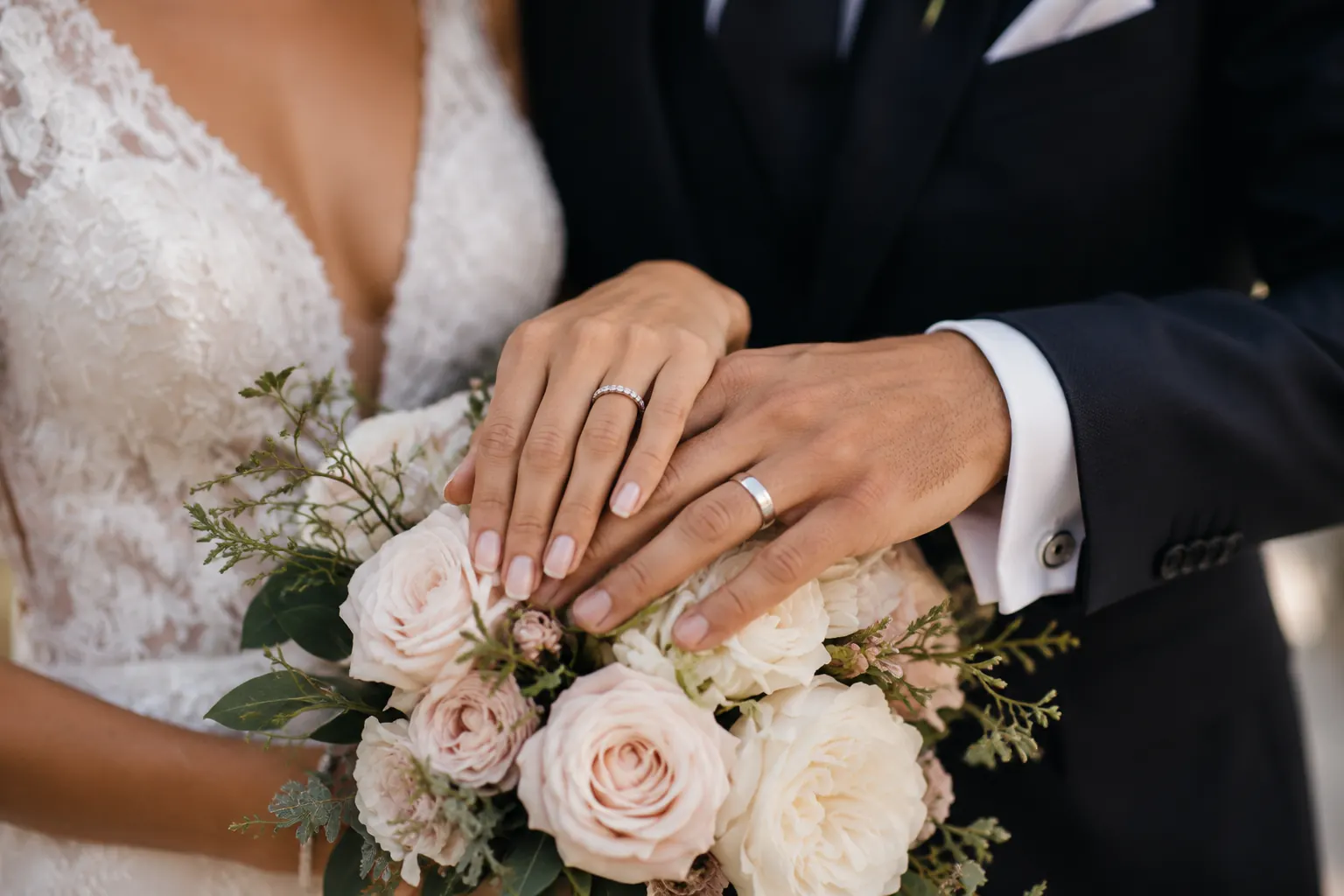 Detalle real de las manos de los novios y los anillos sobre el ramo
